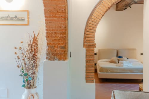 Arco rustico in camera da letto con fiori secchi, mattoni a vista e letto nell'appartamento Tenuta Alela a Figline Valdarno