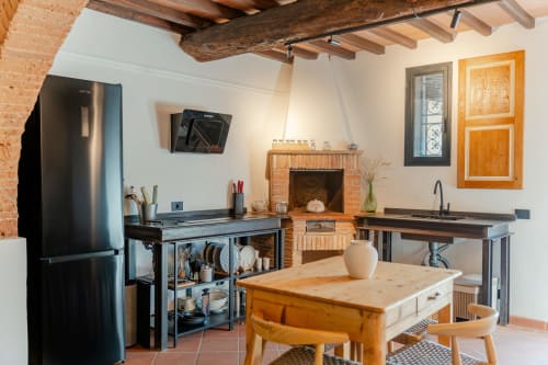 Ampia zona cucina-soggiorno nell'appartamento Tenuta Alela con camino, travi in legno, elettrodomestici in acciaio inox e stile rustico