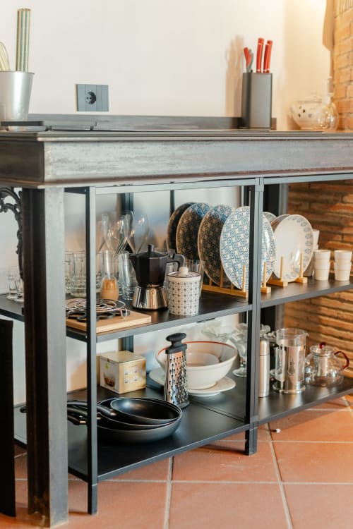 Scaffale cucina industriale presso Tenuta Alela con stoviglie, bicchieri, pentolame e utensili organizzati in stile toscano