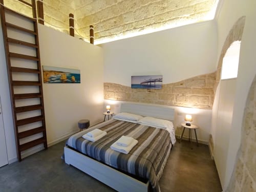 Camera moderna presso il B&B Bari con biancheria a righe, scaffale in legno a scala, e opere d'arte costiera
