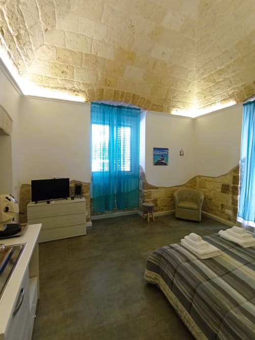 Camera B&B a Bari con soffitto in pietra ad arco, letto, TV, tende turchesi e vista sul mare in Italia