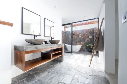 Modern bathroom at La Villa Boz villa with dual stone sinks, mirrors, soaking tub, and natural stone accents