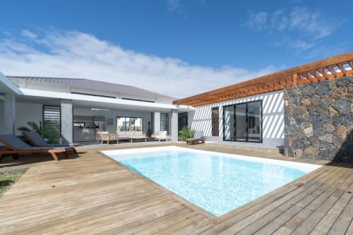 Modern villa with pool, wooden deck, stone accents, and lounge area under blue sky in Saint Philbert de Bouaine