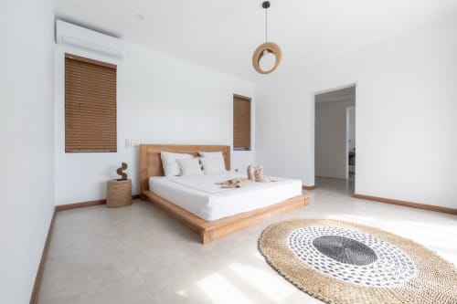 Minimalist bedroom at La Villa Boz with wooden bed, white linens, natural light, woven rug, and wooden accents