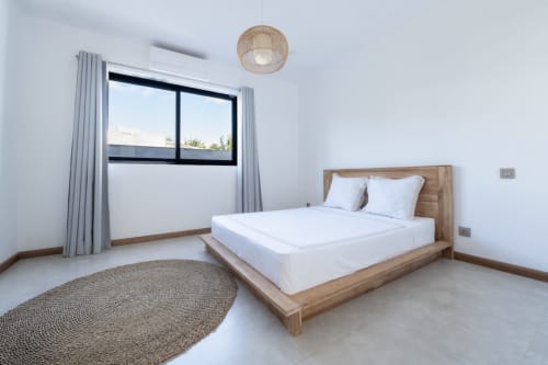 Modern bedroom at La Villa Boz with wooden bed, white linens, woven ceiling light, round jute rug, and window with gray