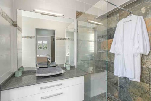 Modern bathroom in Paradise Location villa with double vanity, large mirror, glass shower enclosure, and white robe hanging