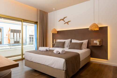 Deluxe double bedroom at Costa Alentejana with ocean-view balcony, modern brown headboard, and coastal decor in Zambujeira do