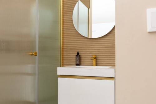 Modern bathroom with white vanity, gold fixtures, circular mirror, and wood-paneled walls in Deluxe room at Alojamento Costa