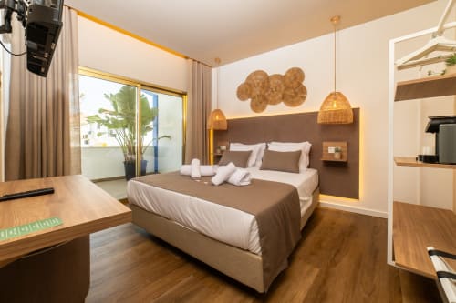 Deluxe double room at Alojamento Costa Alentejana with brown headboard, white bedding, pendant lights, and balcony views in
