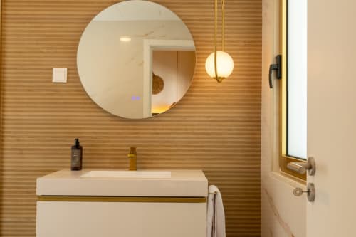 Modern bathroom at Alojamento Costa Alentejana with circular mirror, white sink, and wooden textured walls