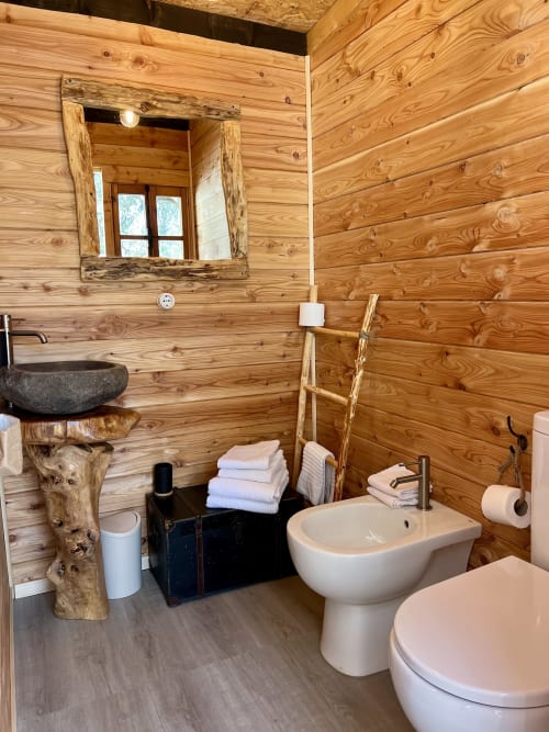 Salle de bains rustique à la Tenda Uliveto d'Agritusmo Stecadò, avec toilettes et bidet blancs, lavabo sur piédestal en pierre