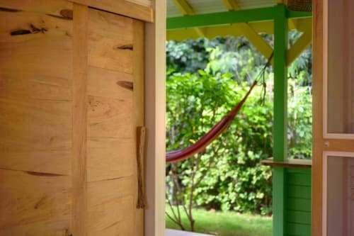 Porte en bois ouverte du gîte Ti'Kaz Lime révélant une vue sur le jardin luxuriant avec feuillage vert et hamac rouge chez Marie et