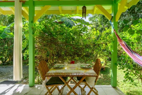 Pergola verte éclatante à Chez Marie et Philippe en Guadeloupe avec table en bois et vues sur le jardin luxuriant