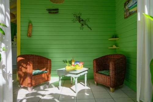 Intérieur de chaumière vert citron éclatant avec deux fauteuils en osier, table d'appoint blanche et vue sur le jardin chez Marie et Philippe,