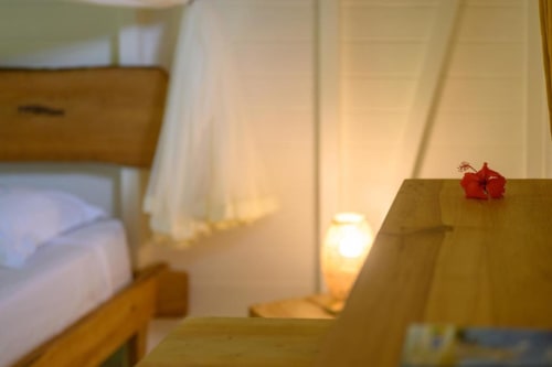 Chambre douillette du gîte Chez Marie et Philippe à Marie-Galante avec mobilier en bois, lumière chaude et fleur rouge