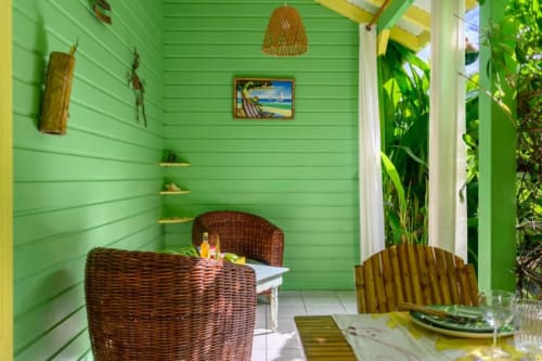 Terrasse lumineuse vert lime du cottage Chez Marie et Philippe, avec mobilier en rotin, plantes tropicales et vue sur le jardin