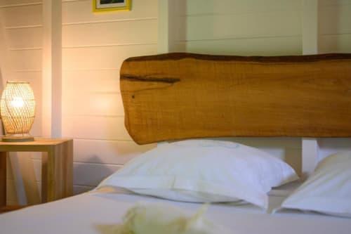 Chambre accueillante chez Marie et Philippe avec tête de lit en bois, oreillers blancs, lampe de chevet et vue sur le jardin à Marie-Galante