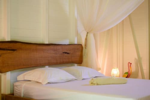 Chambre romantique avec tête de lit en bois, literie blanche, voilages légers et vue sur le jardin à Ti'Kaz Lime.