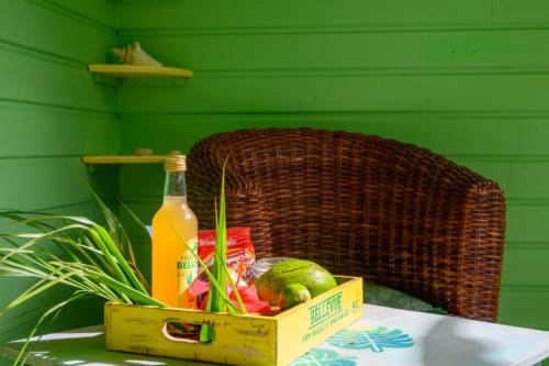 Vue sur le jardin au Chez Marie et Philippe en Marie-Galante avec fauteuil en rotin, plateau jaune en bois, citron vert frais et