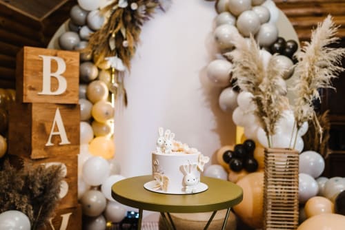 Baby shower celebration setup at Paradise Location with 'BA' wooden sign, white cake with bunny topper, and balloon garland