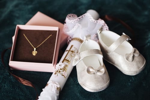 Gold heart necklace, baby shoes, and christening gown on dark teal fabric at Paradise Location Fort-de-France