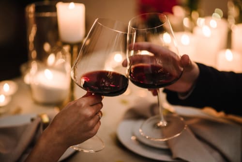 Two people toasting red wine glasses at an elegant dinner with candles at Paradise Location, Fort-de-France