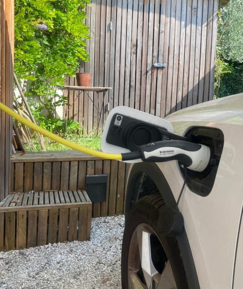White electric car charging at Verdolivo guesthouse in Sale Marasino, with wooden fence and garden backdrop