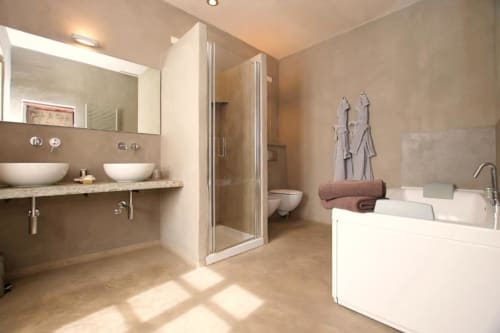 Modern luxury bathroom at Hotel San Giovanni Resort featuring dual vanities, rainfall shower, freestanding bathtub, and warm