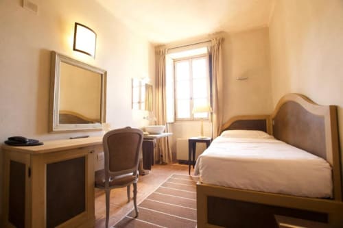 Camera luminosa presso l'Hotel San Giovanni Resort a Saluzzo con letto in legno, scrivania con specchio, finestra con vista sul giardino e
