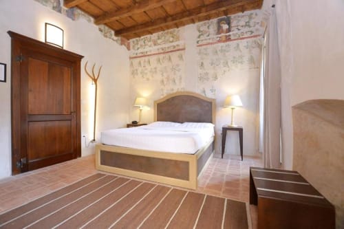 Deluxe room with wooden bed, terracotta floors, and frescoed walls at Hotel San Giovanni Resort in Saluzzo