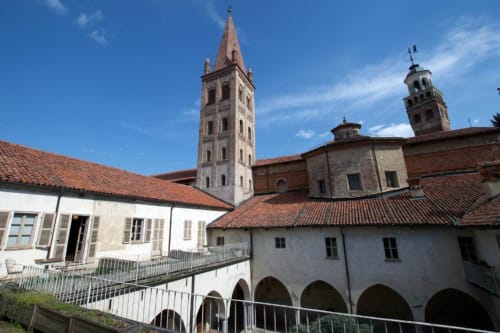 Hotel San Giovanni Resort courtyard with medieval towers in Saluzzo, Italy, featuring arched colonnade and terracotta roofs.