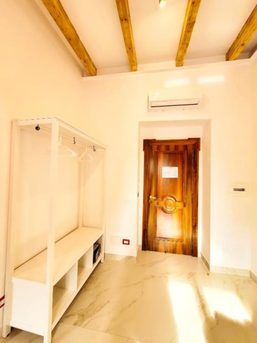 Ingresso della Suite Tripla Lusso a I Migliori Artisti Napoli con porta in legno, armadio bianco, pavimenti in marmo e travi a vista