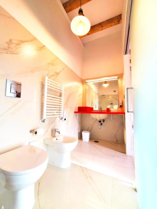 Bagno moderno dell'hotel di lusso I Migliori Artisti a Napoli con pareti in marmo, vanità rossa, toilette, doccia walk-in e sospensioni