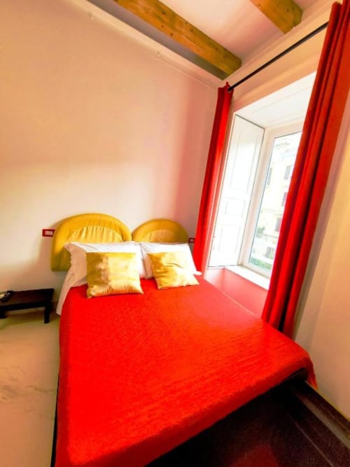 Suite lussuosa a I Migliori Artisti a Napoli con letto rosso, cuscini dorati e vista sulla città dal balcone