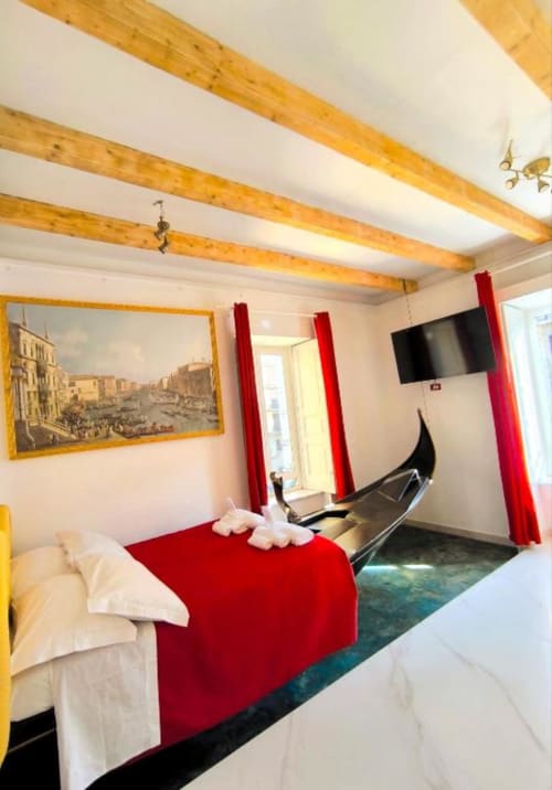 Accogliente camera doppia con travi in legno, biancheria rossa, TV e opere d'arte veneziana presso I Migliori Artisti a Napoli