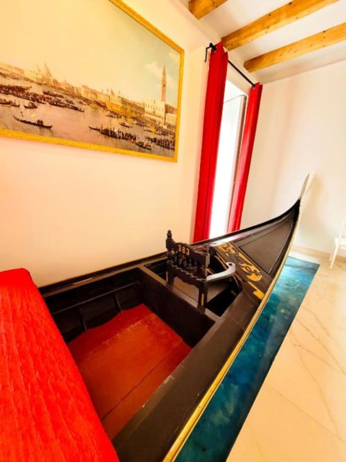 Lussuosa camera con replica di gondola nera, sedute in velluto rosso, opere d'arte veneziana, travi in legno e vista sulla città presso I Migliori