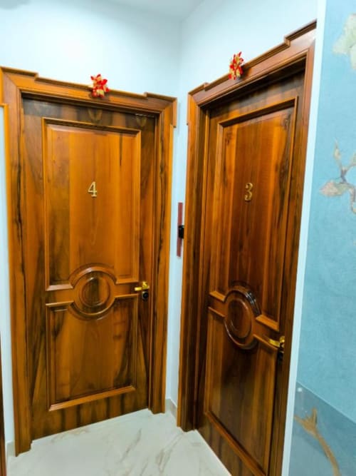 Due porte in legno numerate 3 e 4 in un corridoio di hotel a Napoli con pareti azzurre e fiocchi rossi decorativi