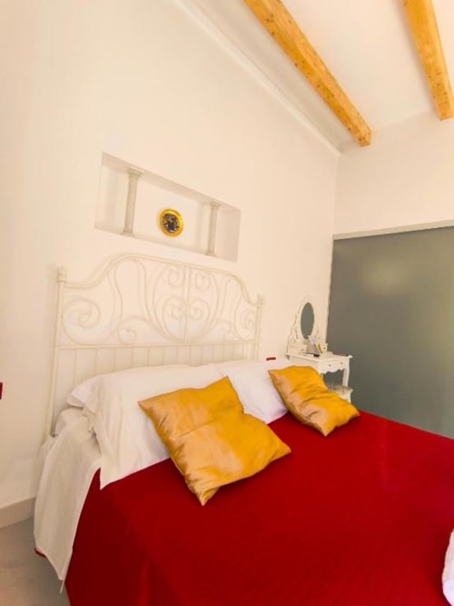 Camera da letto doppia lusso a I Migliori Artisti, Napoli - letto rosso con cuscini dorati, testiera bianca ornamentale, travi a vista