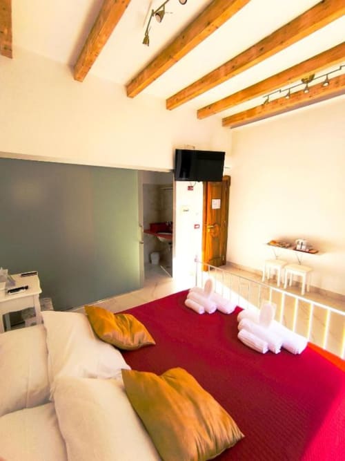 Camera doppia deluxe presso I Migliori Artisti B&B a Napoli con biancheria rossa, travi in legno e vista sulla città