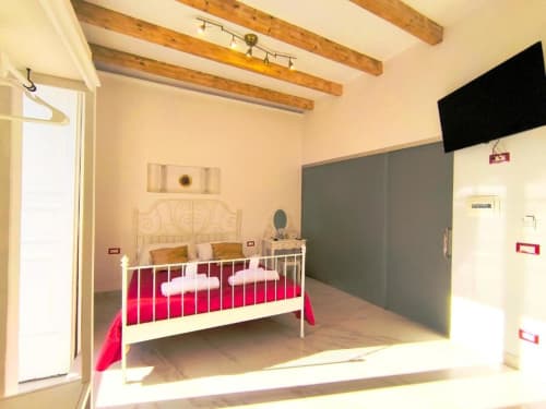 Camera moderna presso I Migliori Artisti B&B a Napoli con letto in metallo bianco, biancheria rosa e travi in legno a vista