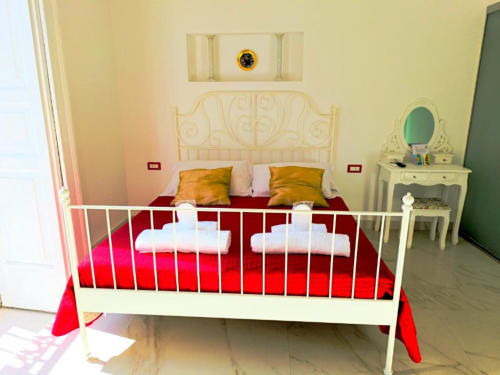 Camera doppia deluxe presso I Migliori Artisti B&B a Napoli con letto in ferro bianco, biancheria rossa e vista sulla città.