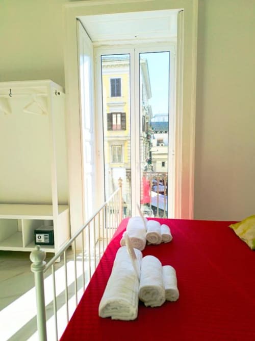Lussuosa camera doppia con coperta rossa, asciugamani arrotolati e balcone con vista sul panorama di Napoli all'I Migliori Artisti boutique