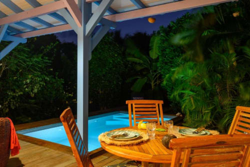 Dîner en terrasse au crépuscule sous pergola avec piscine privée, jardin tropical et chaises orange chez Marie et Philippe