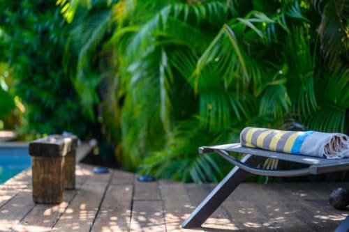 Coin détente au bord de la piscine du gîte Chez Marie et Philippe à Marie-Galante avec serviette rayée et vue sur le jardin tropical