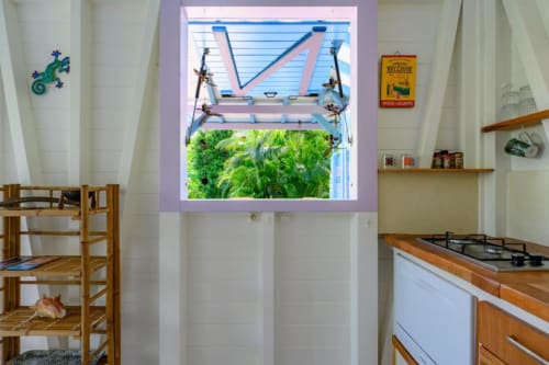 Cuisine lumineuse avec meubles en bois, cuisinière à gaz et fenêtres bleues donnant sur un jardin verdoyant à Chez Marie et Philippe