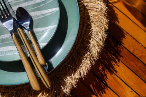 Mise de table élégante à Chez Marie et Philippe, Marie-Galante : fourchette et cuillère aux manches en bois sur assiette turquoise