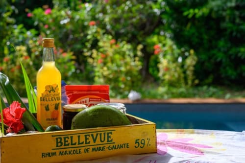 Bouteille de rhum Bellevue et mangue fraîche dans une caisse jaune à la piscine de la villa Chez Marie et Philippe, Marie-Galante