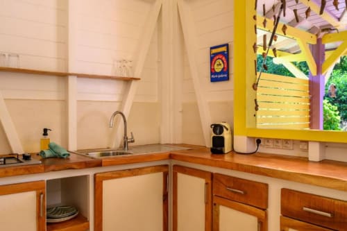 Cuisine moderne avec meubles en bois, évier en acier inoxydable et fenêtre jaune donnant sur le jardin de Chez Marie et