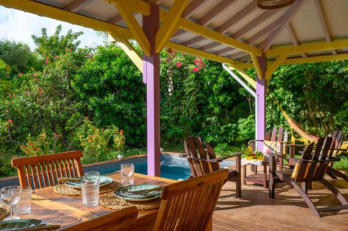 Terrasse couverte avec table de salle à manger en bois et chaises Adirondack vue sur piscine privée et jardins luxuriants de la villa Ti'Kaz Vanille