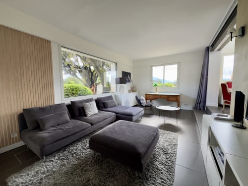 Salon moderne de l'hôtel SoleMare à Alata avec canapé sectionnel gris anthracite, tapis gris et grandes baies vitrées donnant sur les jardins
